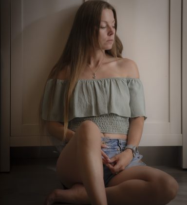 Emotionale Shootings Junge Frau sitzt mit geschlossenen Augen an einer Wand, trägt ein leichtes Oberteil.